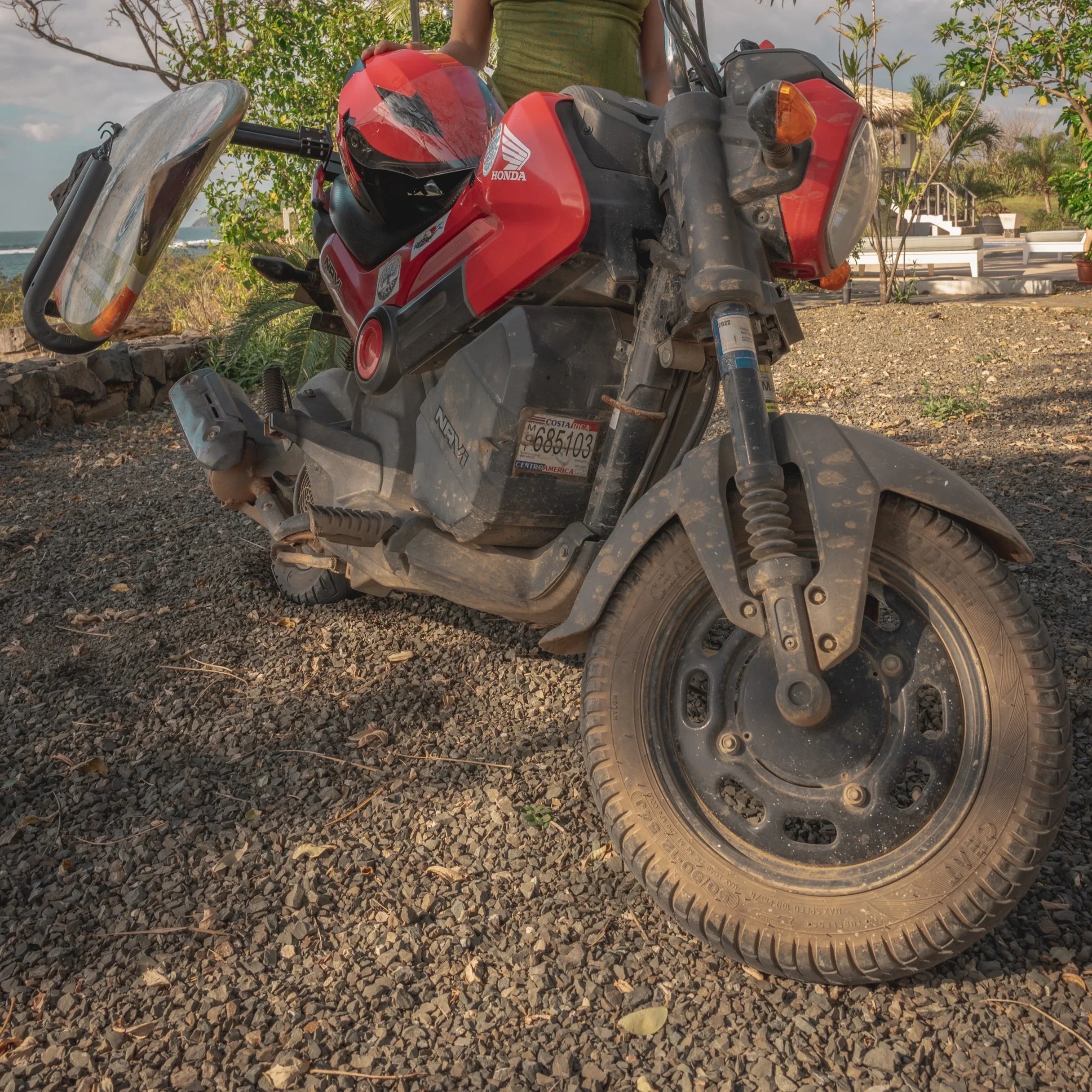 Red Honda scooter with helmet, parked on gravel near beach in Costa Rica