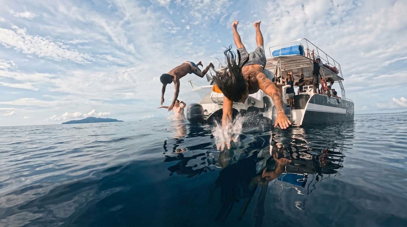 Two people backflipping off a tour boat into flat water