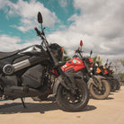 Row of motorcycles parked on a paved surface with a cloudy sky in the background