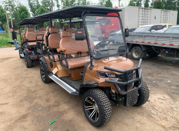 Brown golf cart with multiple seats on a dirt road, with trucks in the background.