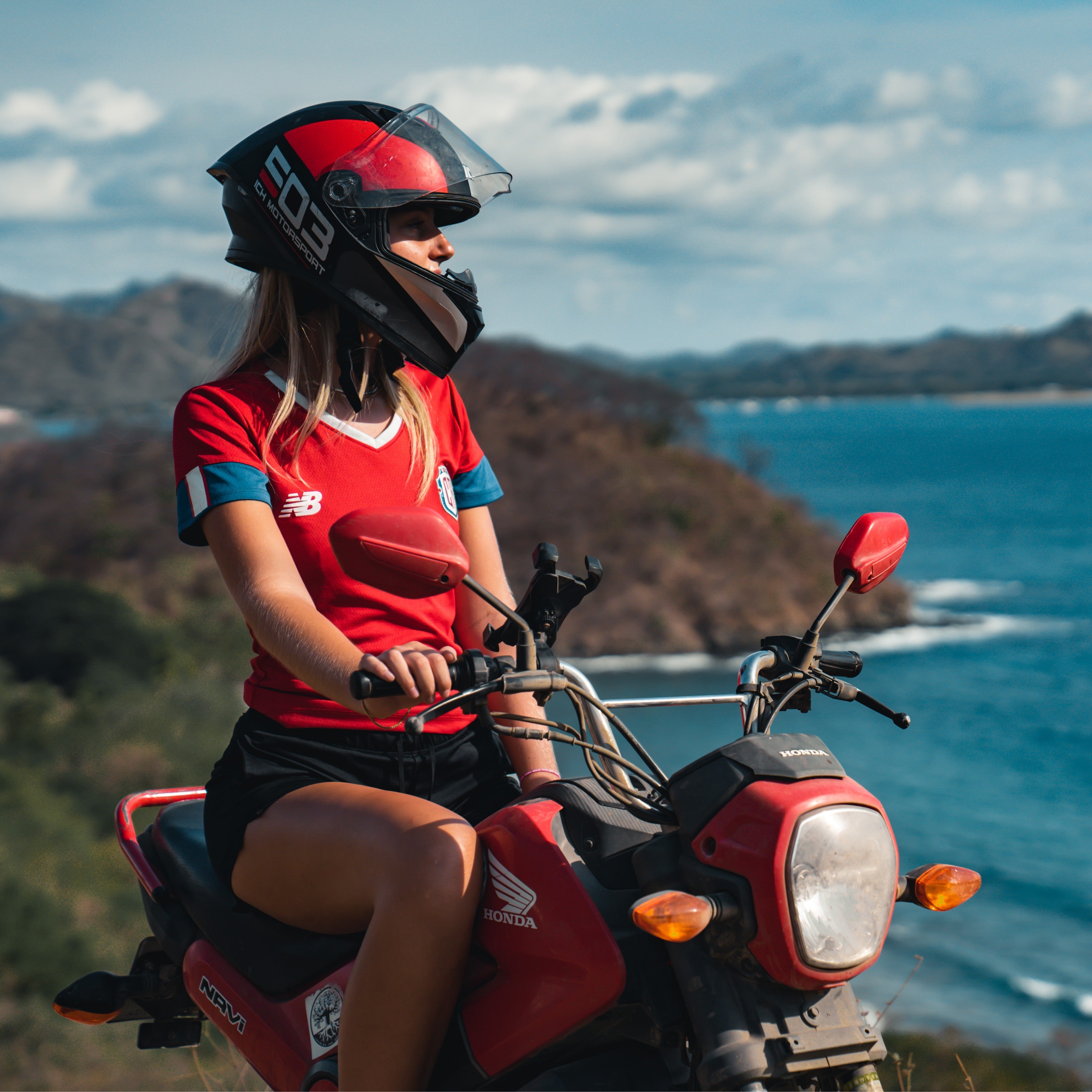 Person on a red motorcycle by the ocean with a scenic background